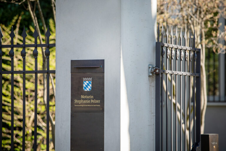 Einfahrt zur Kanzlei mit dem Firmenschild von Notarin Stephanie Pelzer und dem Bayerischen Wappen.