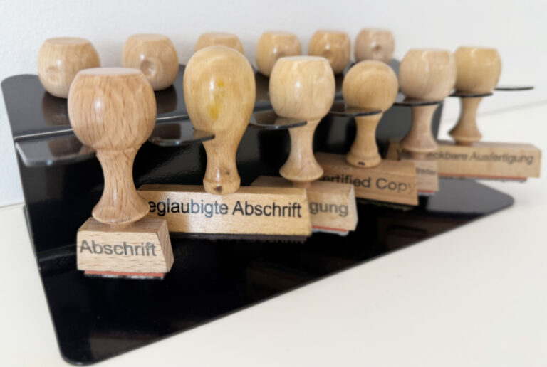 Mehrere Stempel mit Aufschriften wie „Abschrift“, „Beglaubigte Abschrift“ und „Certified Copy“ auf einem Schreibtisch.
